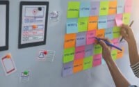 Hands arranging website planning sticky notes and wireframes on a wall